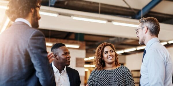 A group of four professionals engage in a discussion in a modern office space, showcasing diversity in business.