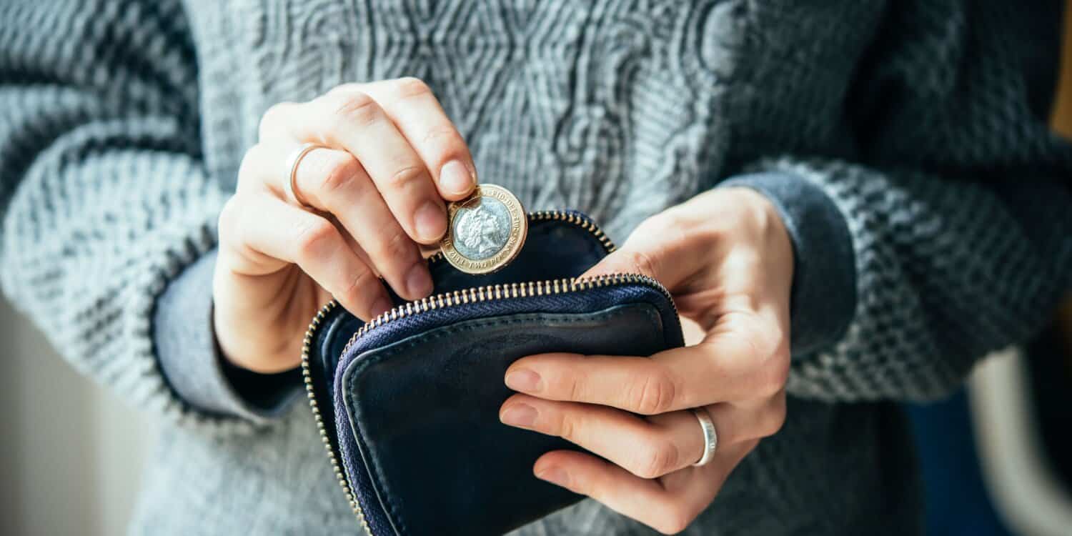 A business owner wearing a grey knitted pullover is placing a pound coin in a purse, illustrating the need for cash reserves.