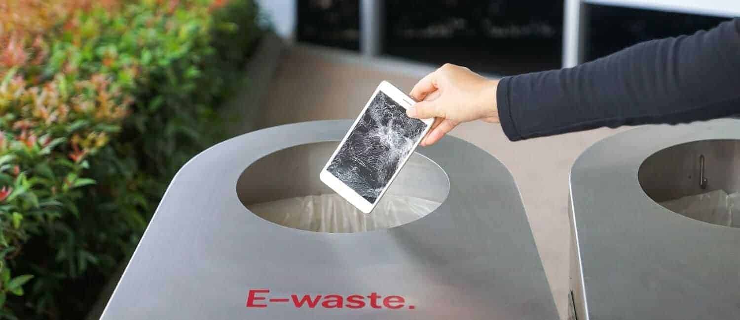 Hand dropping a broken smartphone into a container that is clearly labelled 'e-waste'