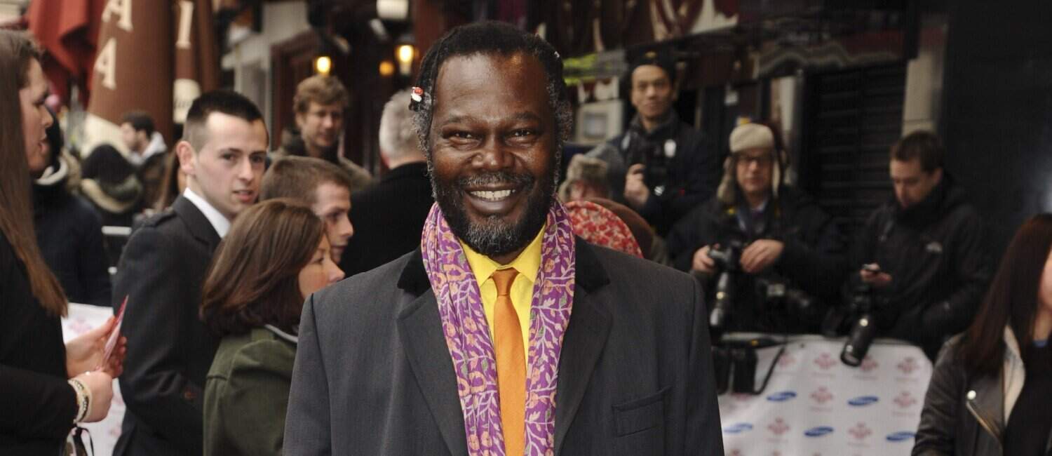 Smiling Levi Roots in a colourful scarf and suit posing at an event, surrounded by people and photographers