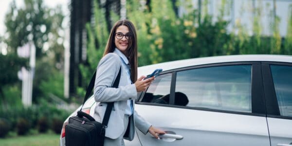 Businesswoman holding a phone and opening the door of a white car, representing the use of a company car and the consideration of benefit-in-kind tax for businesses