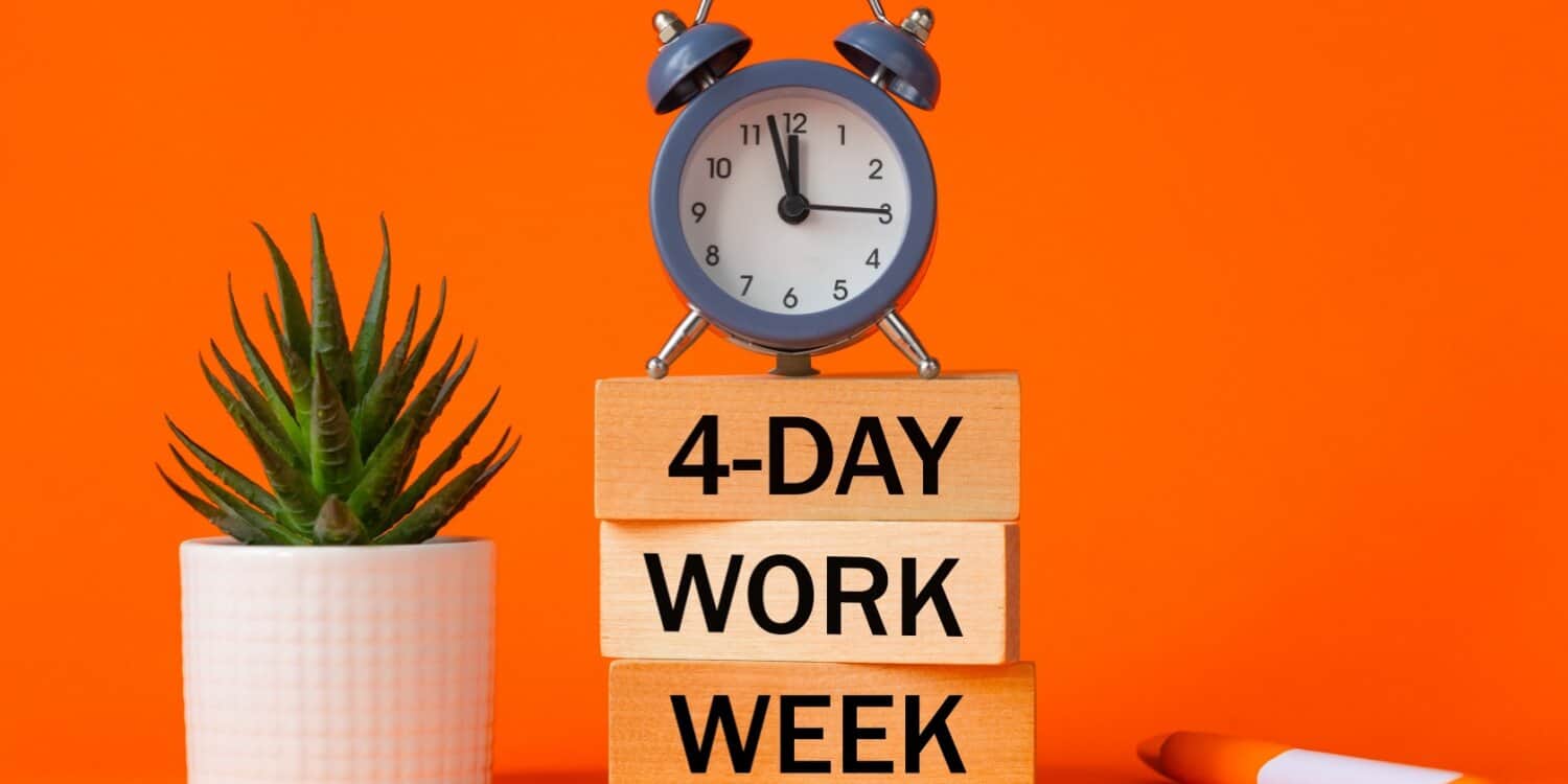 Wooden blocks stacked with the text "4-DAY WORK WEEK" next to a small potted plant and clock, representing the concept of a shorter work week.