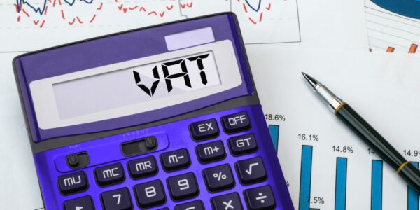 A purple calculator displaying the word "VAT" next to financial charts and a pen, representing VAT registration and accounting for business tax purposes