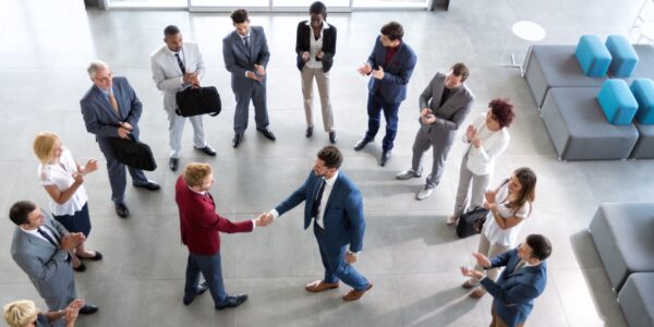 Business professionals in formal attire standing in a circle applauding two men shaking hands — concept of company leadership and directors