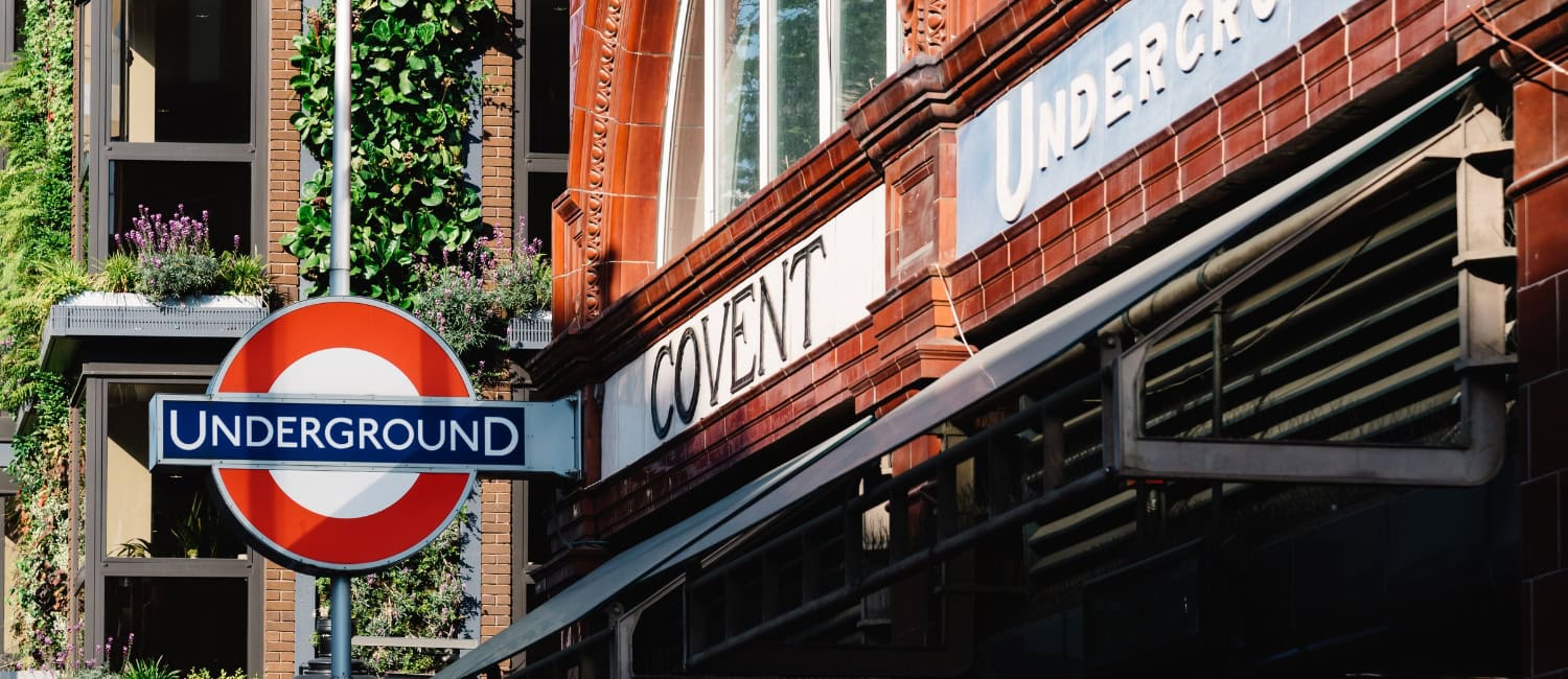 Entrance to Covent Garden Underground Station in London, with a red brick facade and greenery on the adjacent building.