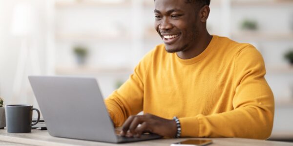 A man wearing a yellow jumper, looking at his laptop and smiling.