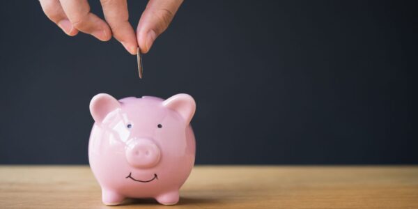 Someone putting a coin into a pink piggy bank.