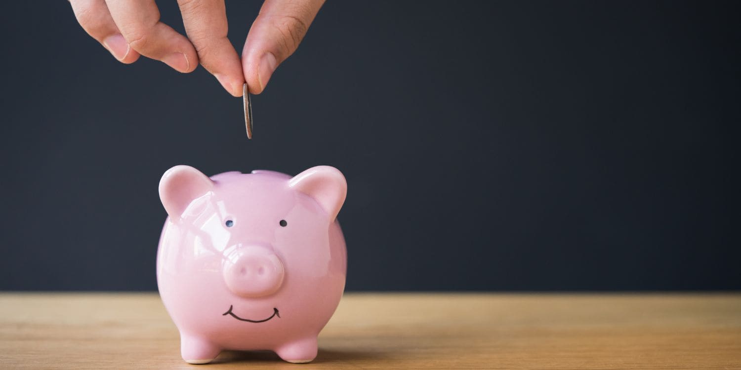 Someone putting a coin into a pink piggy bank.