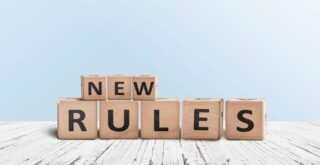 'NEW RULES' sign made of wooden blocks on a desk in a room with a blue background